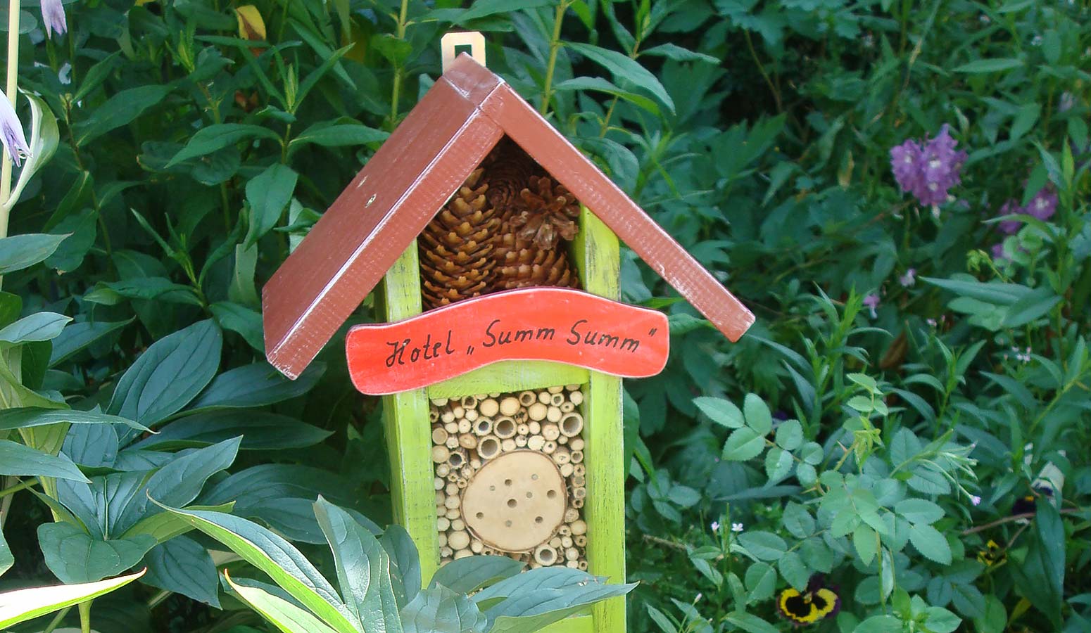 Detailaufnahme aus Andrea’s Garten im Landhotel Klaukenhof mit Insektenhotel und blühender Gartenbepflanzung