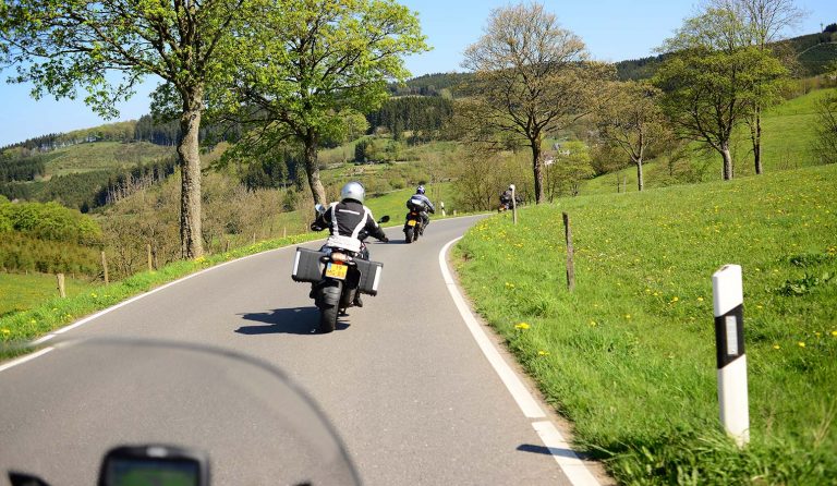 Motorradfahrer auf einer kurvigen Landstraße im Sauerland bei sonnigem Wetter
