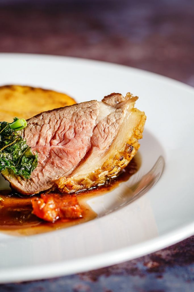 Savor a gourmet duck breast dish with crispy kale and a rich sauce, exquisitely presented on a white plate.