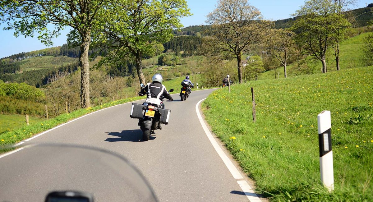 Motorradfahrer auf einer kurvigen Landstraße im Sauerland bei sonnigem Wetter